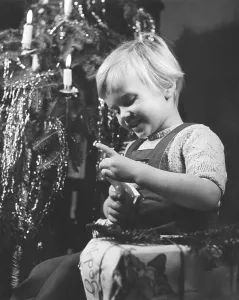 Christmas in the 1940s. A girl is opening her christmas present by the christmas tree