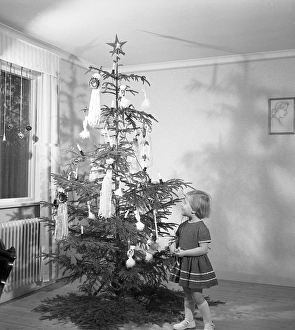 Christmas in the 1950s. A young girl is standing by the christmas tree