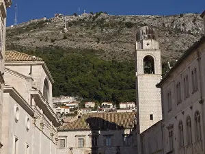 Church bell tower and historic buildings in front of a wooded mountain and blue sky