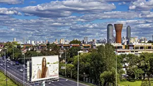 Cityscape with skyscrapers, a large billboard and busy traffic under a cloudy sky