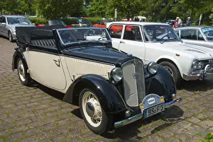 Classic black and white vintage car in an open-air car park with other vintage cars in the background