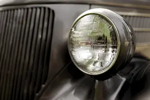 Detail of a classic car's headlight with chrome finish on a dark body in St