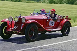 A classic red vintage car with two drivers on a country road