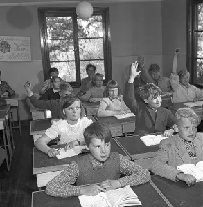 A classroom in 1952. Interior of a classroom where a class is sitting neatly in their school desks. The desks had a lid that could be opened. In the drawer underneath, the schoolgirls kept their books, pencils and school supplies
