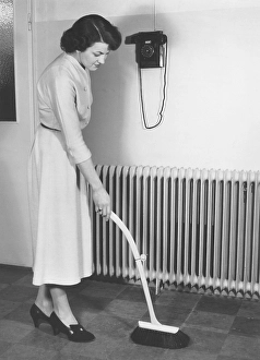 Cleaning day in the 1940s. A young woman is cleaning her apartment and is using a bush with an telescoping handle