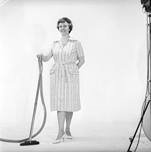 Cleaning day in the 1960s. A woman is standing holding a vacuum cleaner