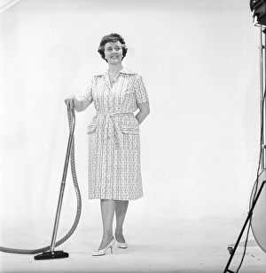 Cleaning day in the 1960s. A woman is standing holding a vacuum cleaner