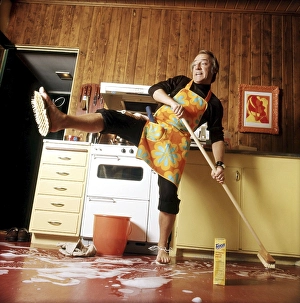 Cleaning day in the 1970s. An interior of a kitchen where a man is seen cleaning the floor