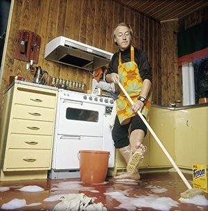 Cleaning day in the 1970s. An interior of a kitchen where a man is seen cleaning the floor