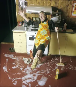 Cleaning day in the 1970s. An interior of a kitchen where a man is seen cleaning the floor