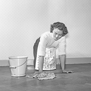 Cleaning the floor back then. A young woman is lying on the floor and use a scrubbing brush to get the floor clean
