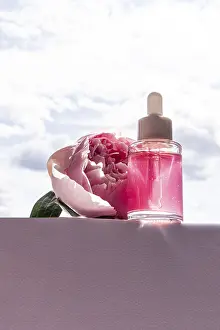 A clear cosmetic bottle filled with pink liquid sits elegantly beside a blooming pink peony