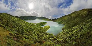 A clear lake surrounded by green hills and mountains under a blue sky with clouds on a sunny day