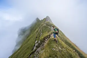 Climbers on a narrow ridge, steep grassy mountains in the fog