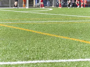 Close up of a green artificial texture soccer field with bright white and yellow lines