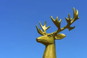 Close-up of a golden deer sculpture in front of a bright blue sky