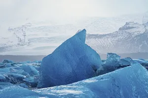 Close-up of a large blue iceberg against a mountainous background