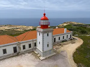 Close-up of a lighthouse and a neighbouring building overlooking the sea under a cloudy sky Aerial view