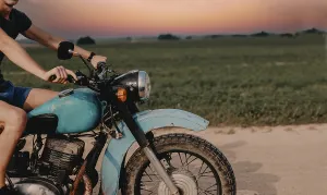 Close-up of a person riding a blue motorcycle on a road during sunset