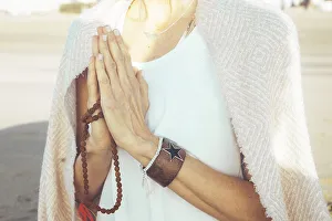 Close up of a woman clasping hands while holding a japa mala outdoors