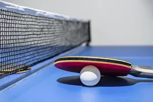 Closeup red table tennis racket and a white ball on the blue ping pong table with a black net