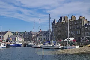 Coastal harbour with sailing boats and historic buildings under a bright blue sky