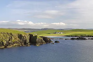 Coastal landscape with cliffs and green land under a slightly cloudy sky