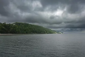 Coastal landscape with densely wooded hills and steep cliffs under a dramatically cloudy sky