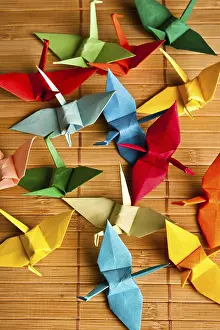 Colorful origami paper cranes scattered on a bamboo mat