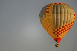 A colourful hot-air balloon floats gently through the clear sky as the sun slowly sets on the horizon