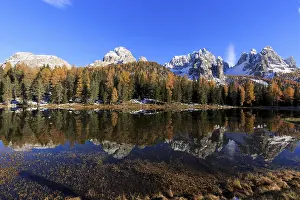 The colourful scenery of an autumnal forest next to a mirror-smooth lake in the sunlight