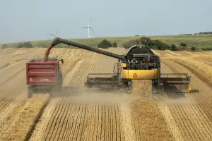 Combine harvester on a wheat field empties harvested barley onto a following tractor with a wagon at Ystad