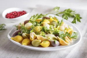 Conchiglie colored pasta with fresh greengrocery on a linen tablecloth on white wooden background
