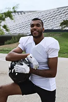A confident American football player in uniform poses outdoors