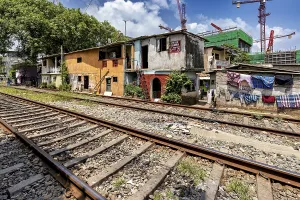 Framed Print : Construction cranes rise behind brightly painted houses along the train tracks under a blue sky