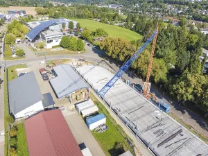 Construction site under blue sky with crane in urban environment and many trees