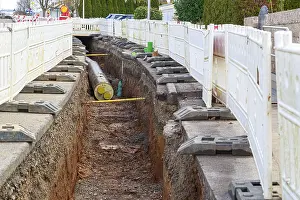 Construction site scene with district heating pipeline in a deep trench and white barriers