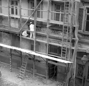 Two construction workers renovate the facade of a house around 1950