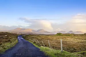 Empty country road between meadows leading to mountains in far distance