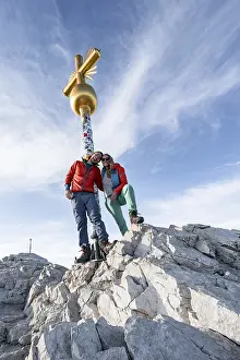 Couple, two mountaineers in front of a golden summit cross