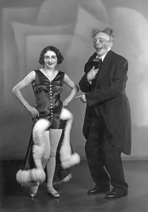 Couple on stage, a clown making fun of a woman in a fashionable dress