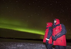 Couple, woman and man, watching green northern polar lights (Aurora borealis)