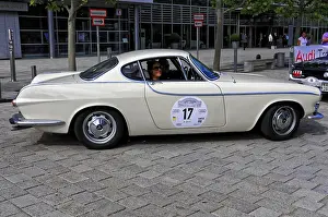 Cream-colored classic car with classic lines and drivers in an urban road environment