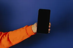 Crop hand of anonymous person holding smartphone with black screen against blue background