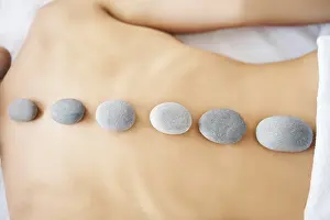 Cropped close up female relaxing in spa salon with hot stones on her back