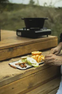 Cropped, unrecognizable person slices fresh oranges and apples