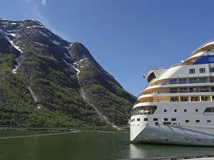 A cruise ship against a majestic mountain backdrop with a clear blue sky