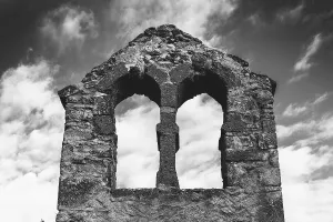 Crumbling stone ruins of a bell tower stand against a cloudy sky