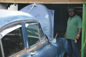 Cuban standing next to his car as it is serviced