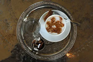Cup of Cappuccino, glass of water and sugar sachets served on a round silver tablet with engravings